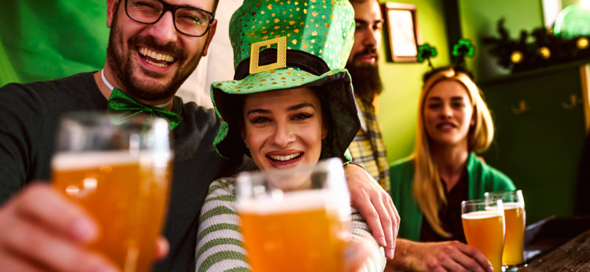 Smiling young people drinking craft beer in pub on St Patrick's Day holiday