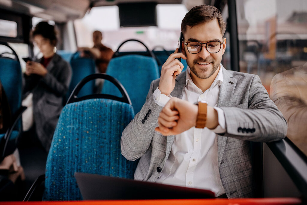 A man looking at his watch on his wrist talking on the phone sitting in a bus