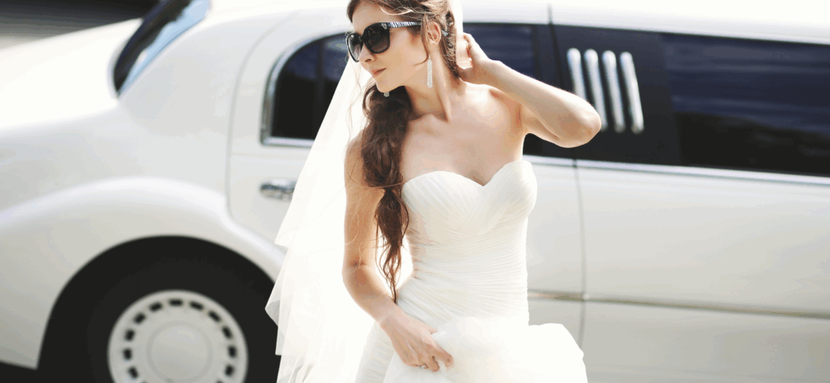 A bride in a wedding dress with sunglasses posing in front of a Dream Limousine